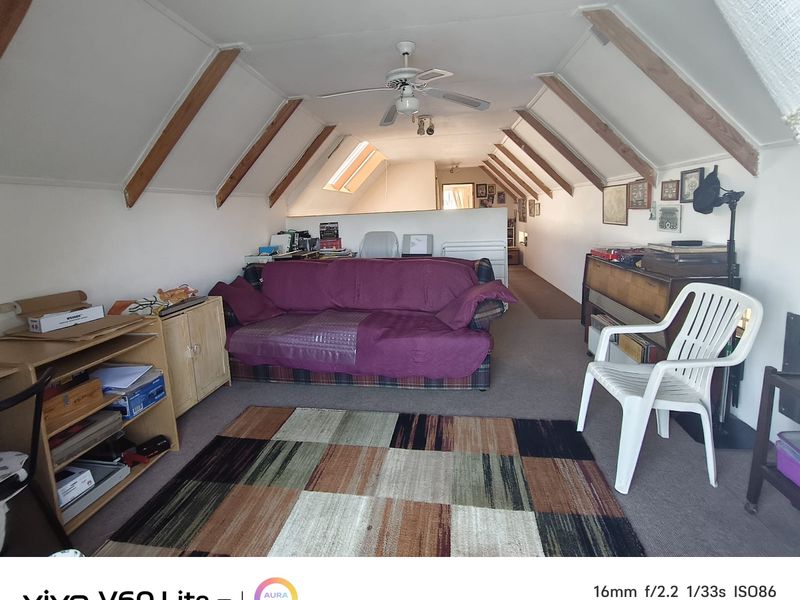 An attic-style living room featuring exposed timber rafters, a ceiling fan, and skylights, offering a unique architectural space with potential for modernization.