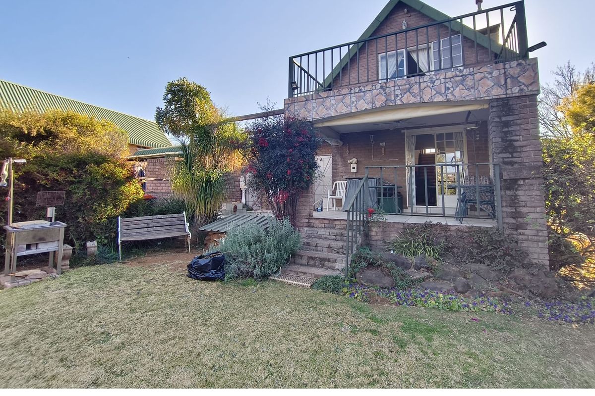 Rear view of a two-story brick house featuring a stone-clad balcony, patio area, and established garden space.