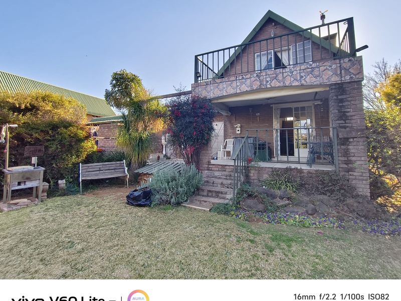Rear view of a two-story brick house featuring a stone-clad balcony, patio area, and established garden space.