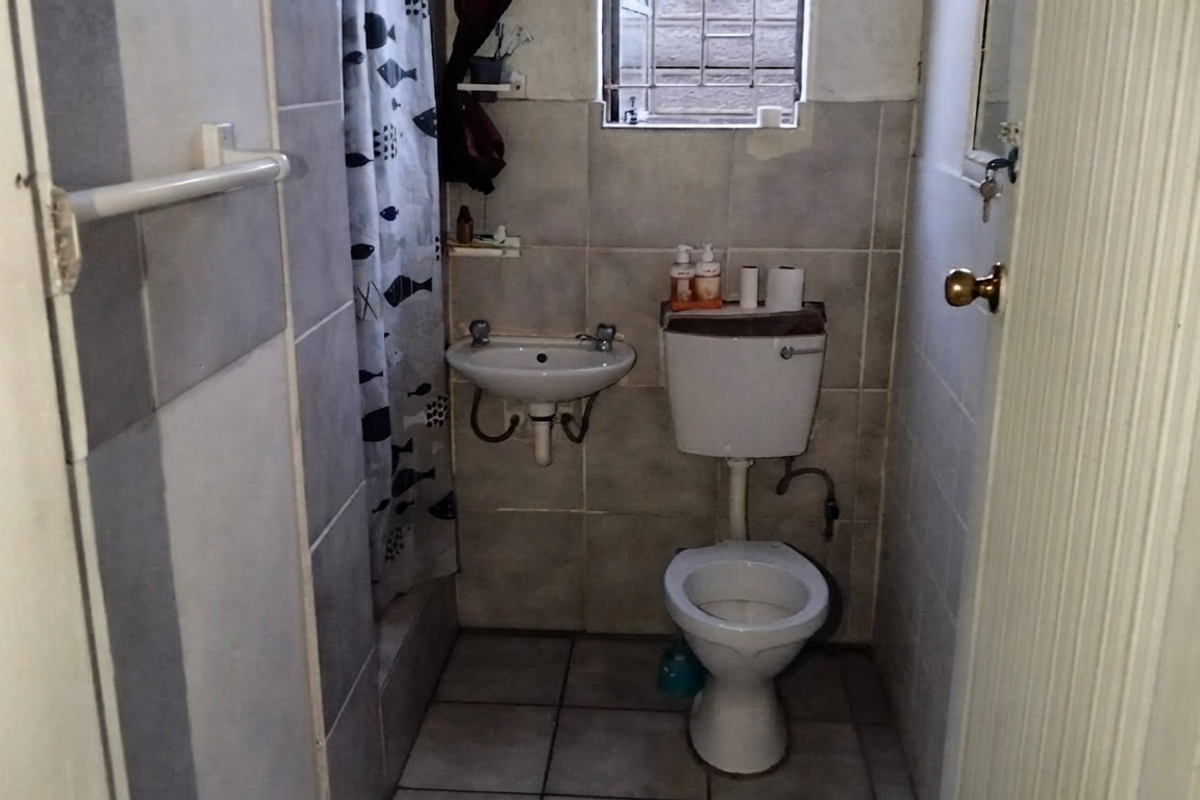 Compact bathroom featuring a wall-mounted basin, toilet, and tiled finishes. The space requires cosmetic updates to improve its overall condition and appeal.