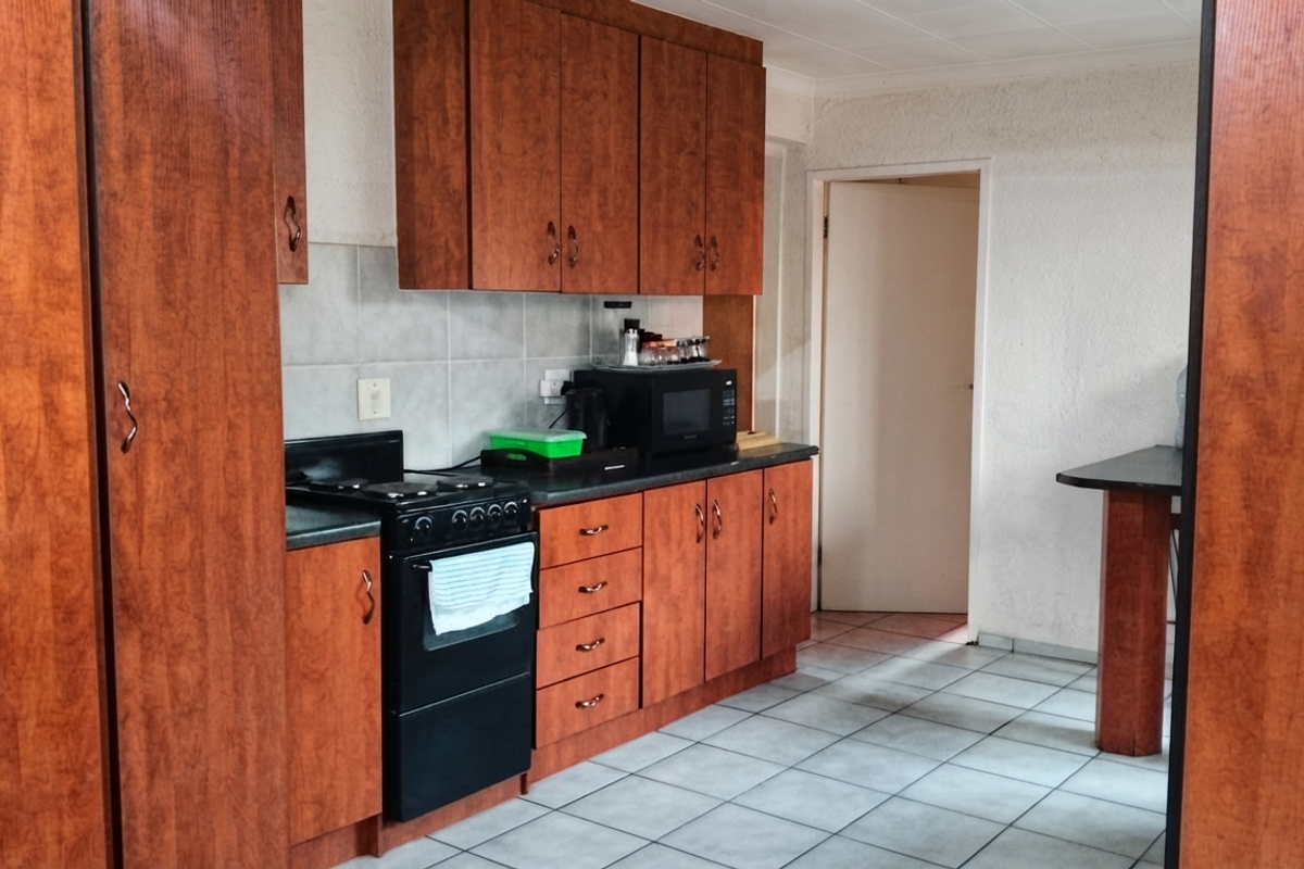 A functional kitchen featuring wood-look laminate cabinetry, tiled flooring, a tiled backsplash, and a built-in breakfast bar area.