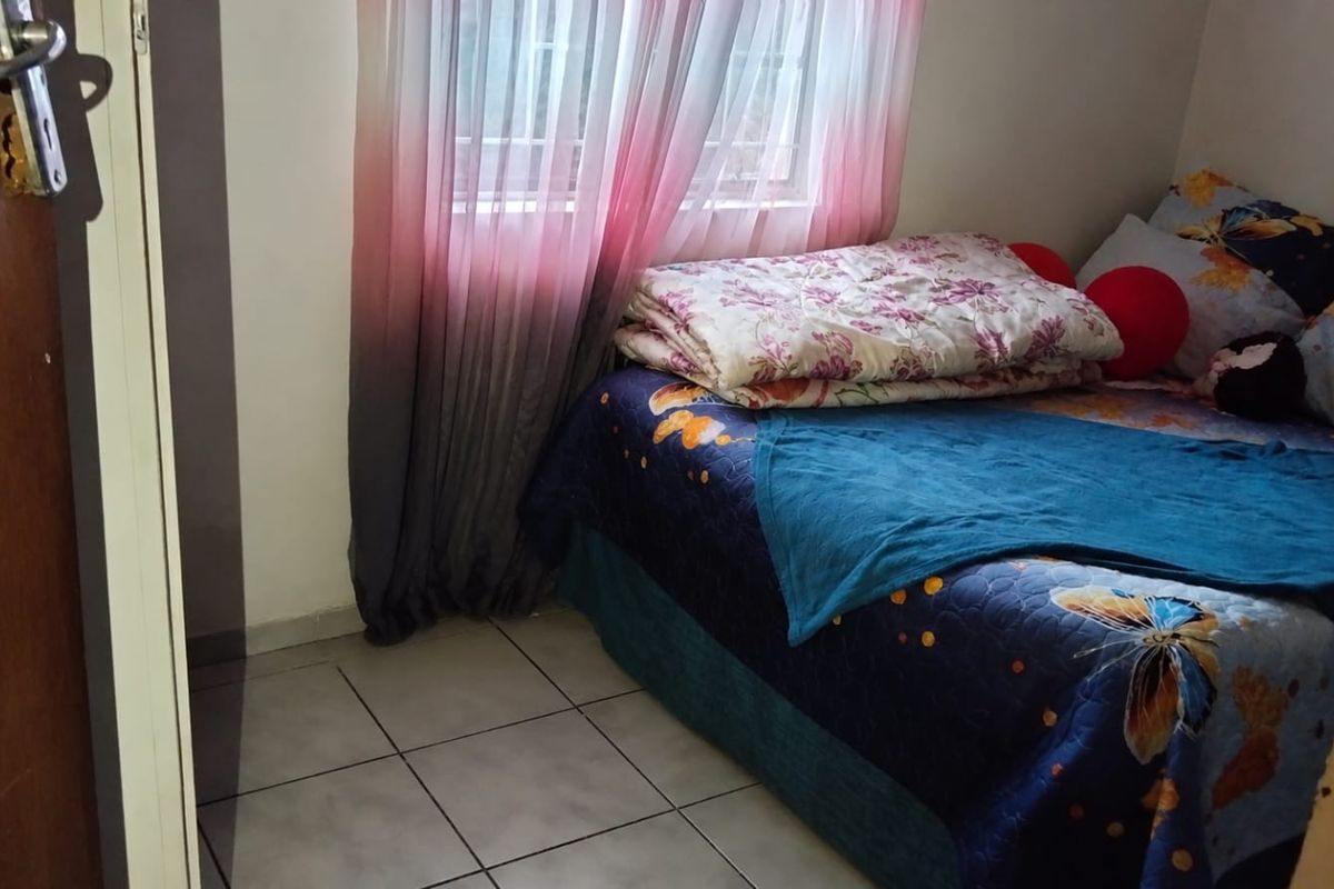 A compact bedroom featuring tiled flooring and a window fitted with security bars.