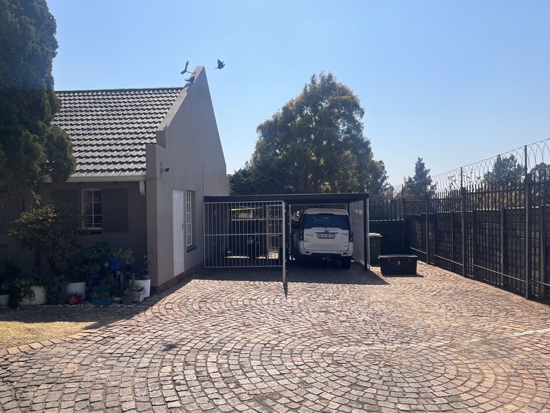 Front exterior view of the townhouse featuring a paved driveway, a covered carport, and secure perimeter fencing.