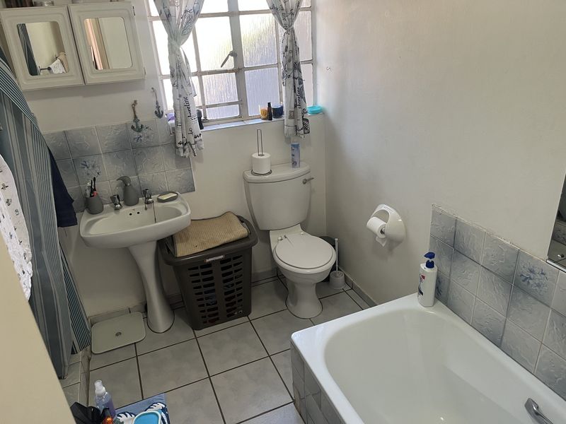 A functional bathroom featuring a pedestal basin, toilet, and bathtub with tiled splashbacks and flooring, offering potential for a modern renovation.