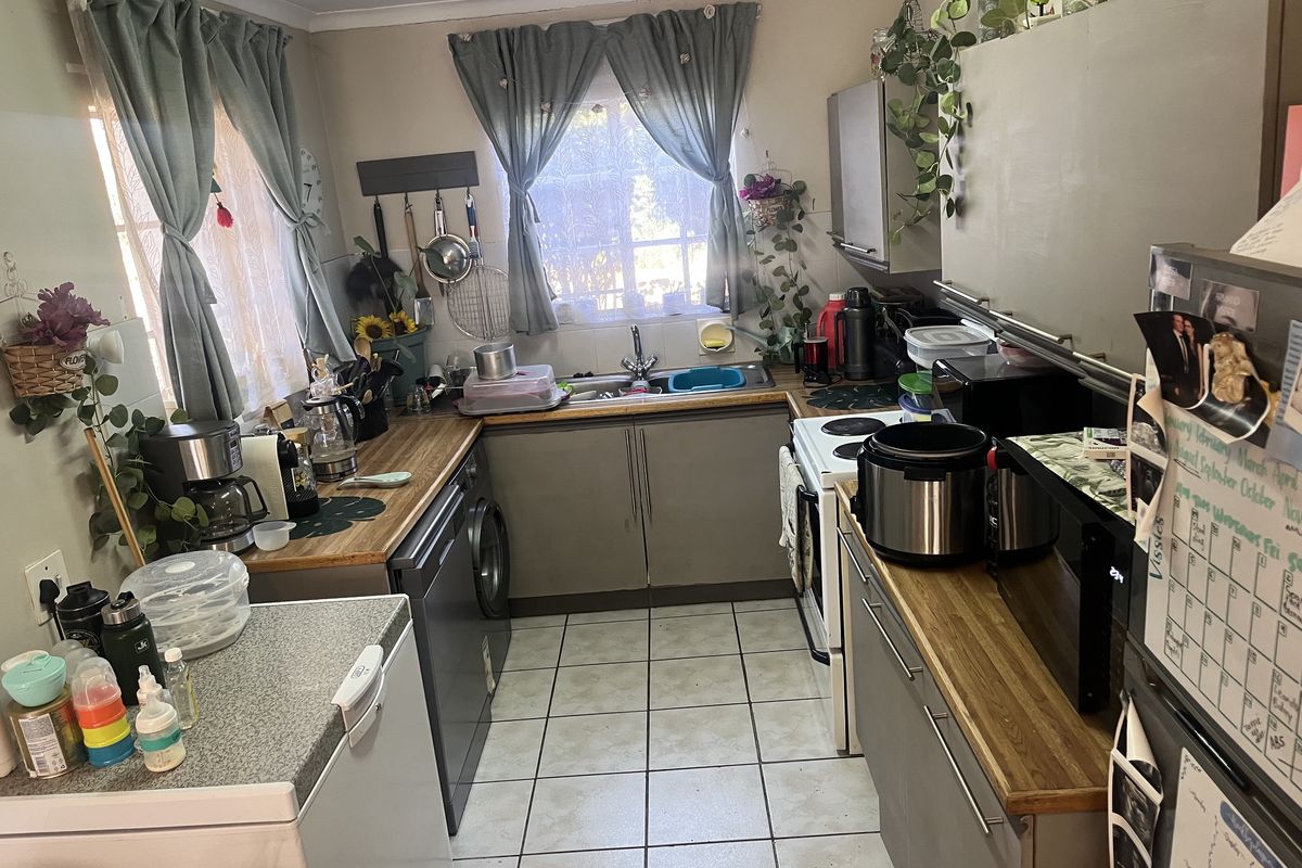 A functional kitchen featuring tiled flooring, laminate countertops, and built-in cabinetry with a double sink and electric stove.