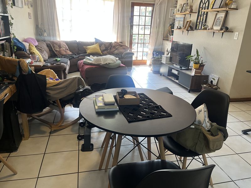 Open-plan living and dining area featuring tiled flooring, natural light from a large window, and access to the exterior via a glass panel door.