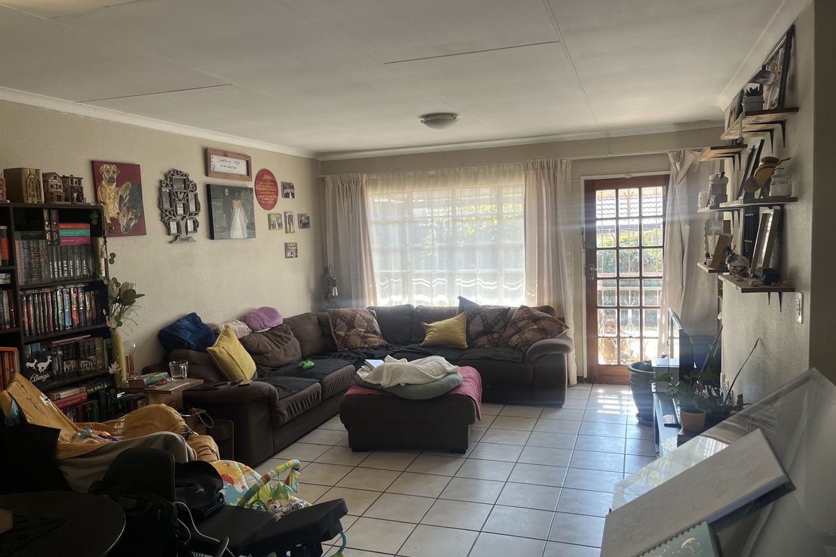 A spacious living room featuring tiled flooring, coved ceilings, and a glass panel door providing access to the outdoor area.