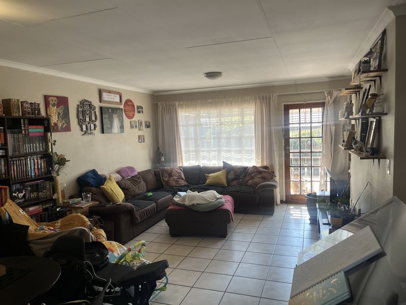 A spacious living room featuring tiled flooring, coved ceilings, and a glass panel door providing access to the outdoor area.