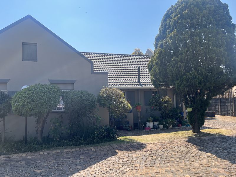Front elevation of a townhouse featuring a paved driveway, tiled roof, and exterior shutters, set within a landscaped garden area.