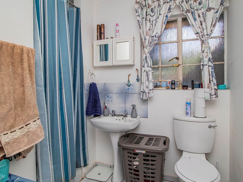 A compact bathroom featuring a pedestal basin, toilet, and shower area with a curtain, requiring modernization of finishes and fixtures.