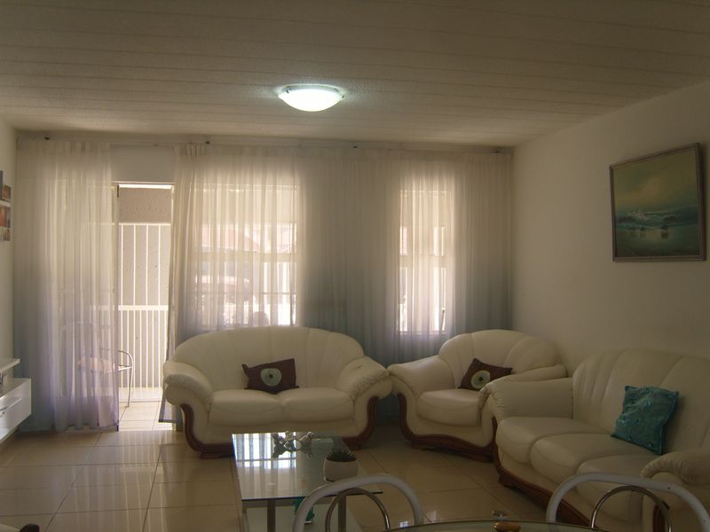 A living room featuring tiled flooring, a ceiling light fixture, and a sliding glass door leading to an outdoor area with a security gate.