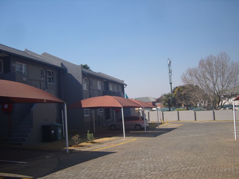Exterior view of an apartment complex featuring paved parking areas with shade cloth carports and a perimeter boundary wall.