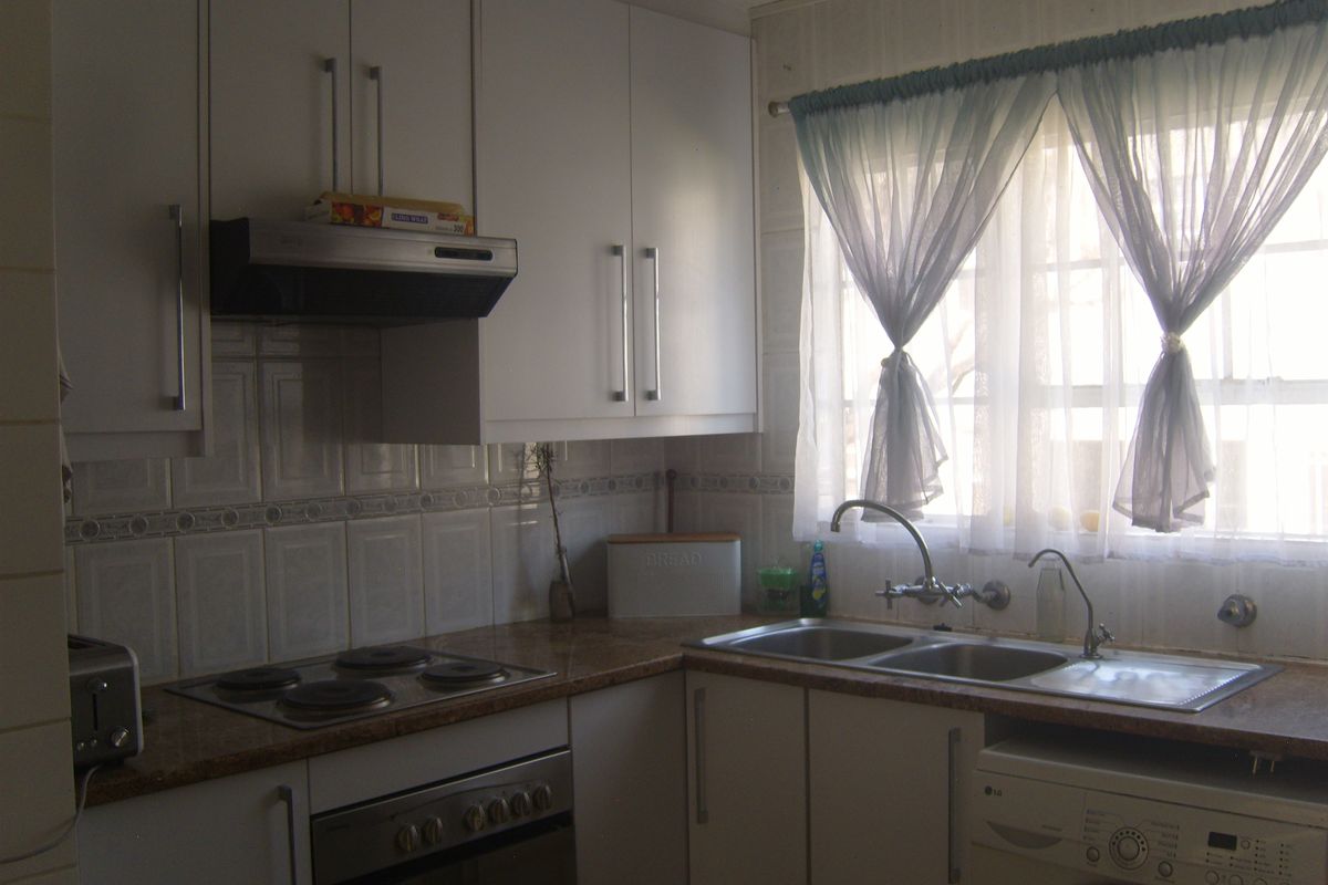 Functional kitchen featuring white cabinetry, laminate countertops, integrated electric hob, oven, extractor fan, and a double bowl sink with tiled backsplash.