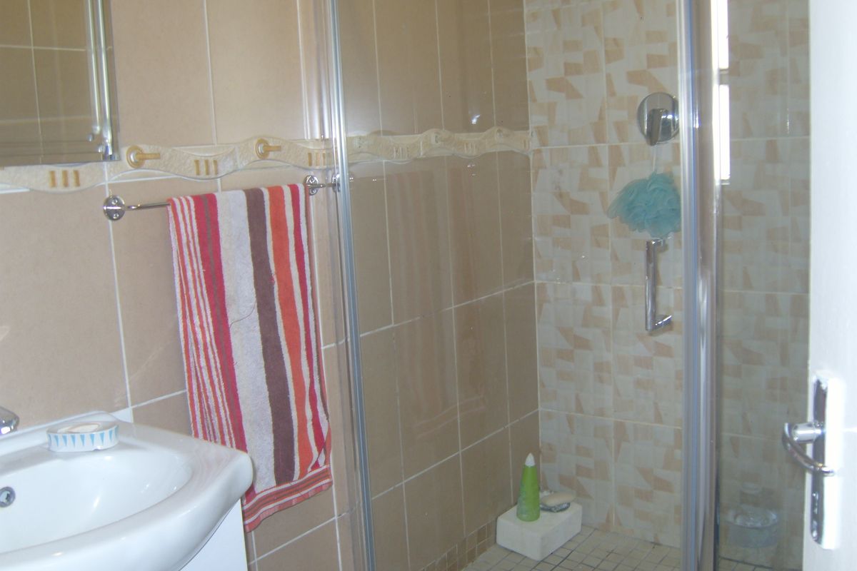 A functional bathroom featuring a tiled shower enclosure, vanity basin, and neutral wall tiling throughout.