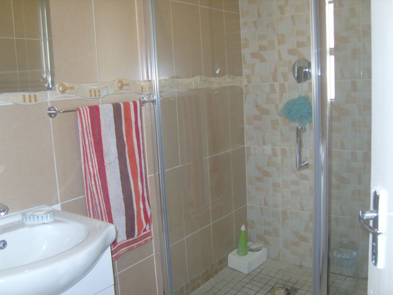 A functional bathroom featuring a tiled shower enclosure, vanity basin, and neutral wall tiling throughout.