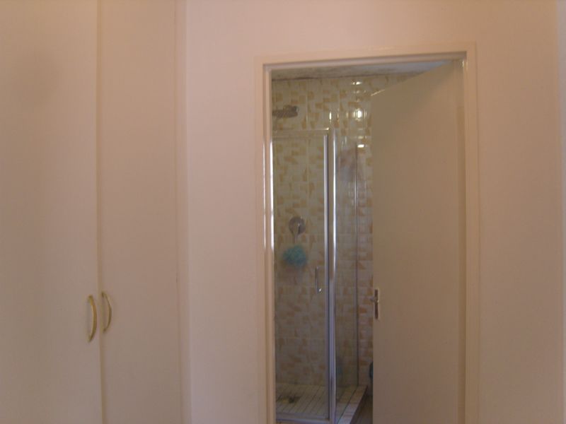 A bathroom featuring a shower enclosure with tiled walls, adjacent to built-in storage cupboards.