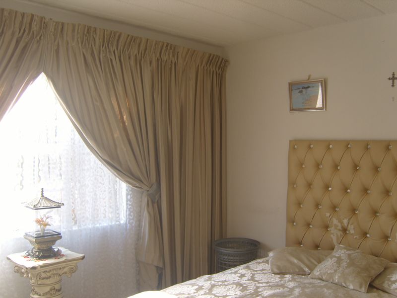 A bedroom featuring a textured ceiling and full-length curtains, providing a neutral base for potential interior updates.