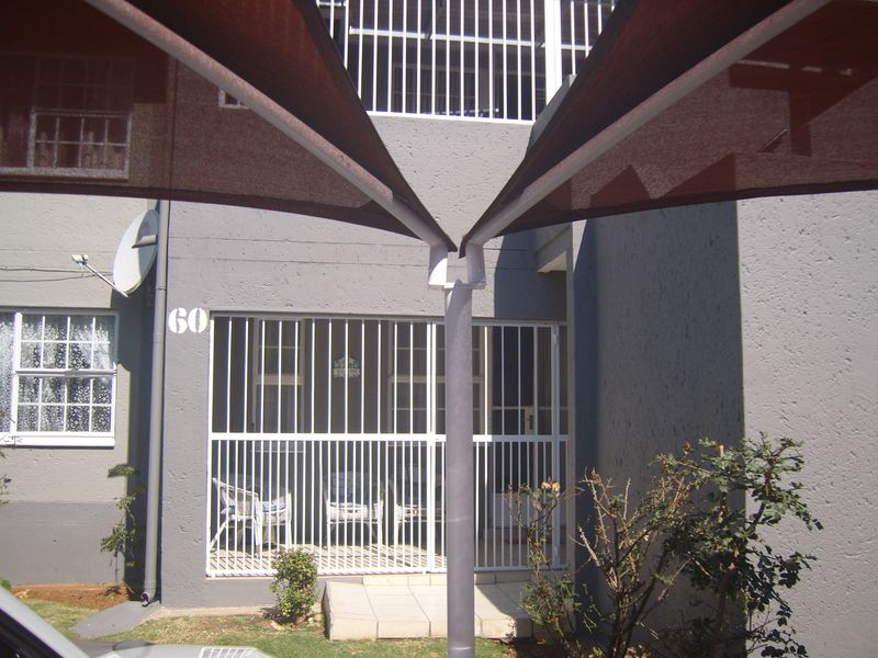 Front entrance of the apartment featuring a shade sail, security gate, and security bars over the windows and entrance.