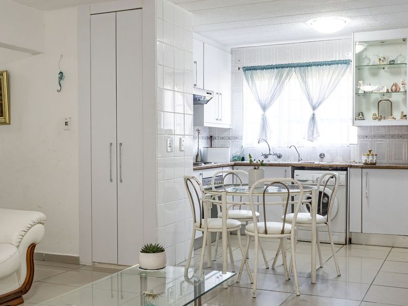 Open-plan kitchen and dining area featuring white cabinetry, tiled backsplash, and neutral floor tiles, offering a functional and bright living space.