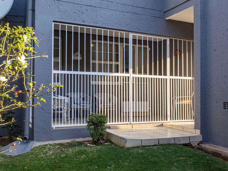 A ground floor patio area featuring a white security gate, tiled flooring, and direct access to the garden space.