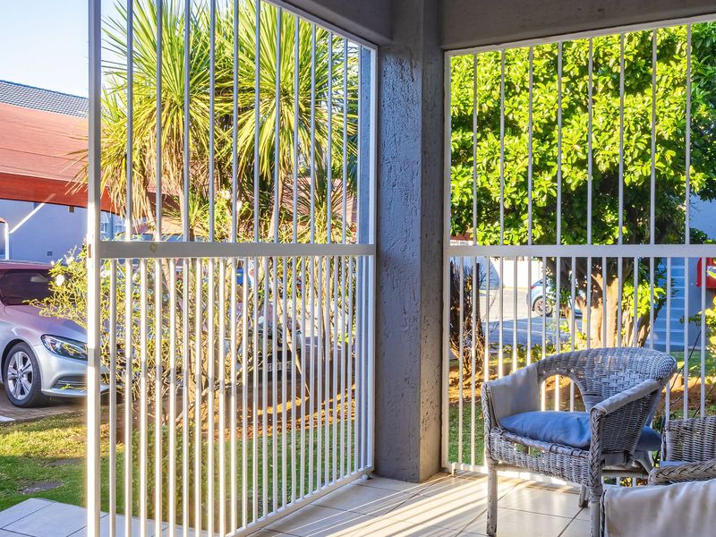 A covered patio area featuring tiled flooring, concrete structural pillars, and white security bars overlooking a parking area.