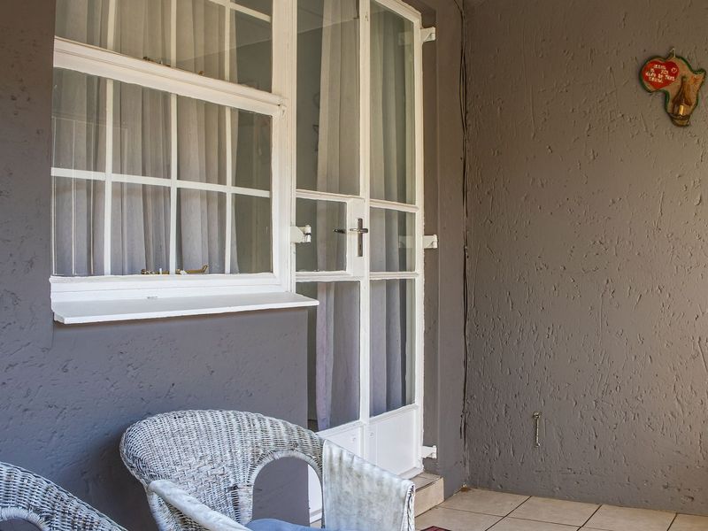 A covered patio area featuring tiled flooring, textured walls, and access to the interior through a multi-pane glass door and window.