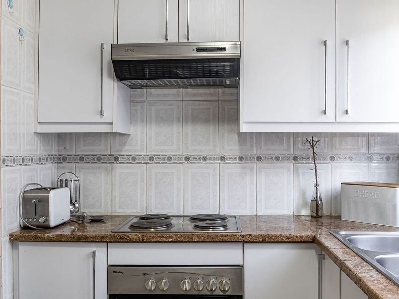 A functional kitchen featuring white cabinetry, granite countertops, a tiled backsplash, and integrated appliances including an oven, hob, and extractor fan.