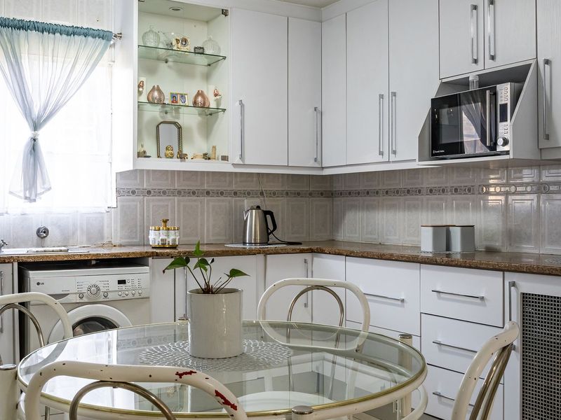 A functional kitchen featuring white cabinetry, granite countertops, tiled backsplash, and integrated appliances including a washing machine and built-in microwave.