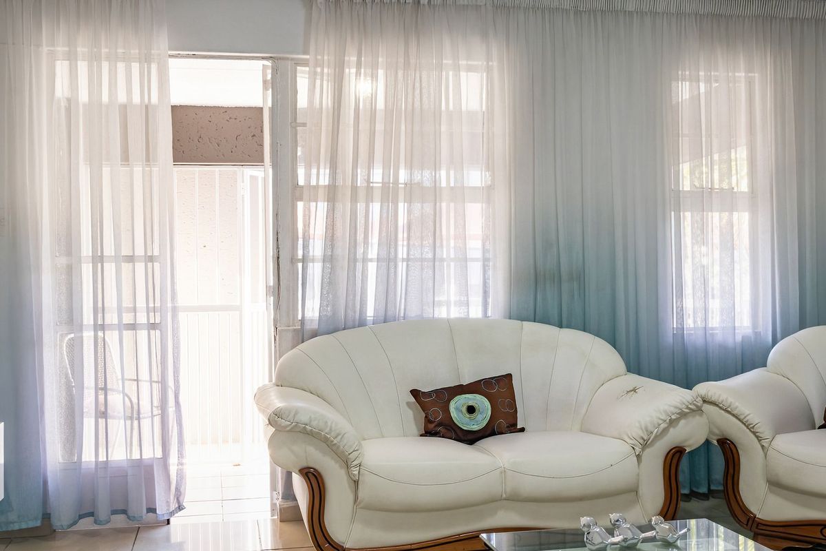 A bright living room featuring tiled flooring and a sliding glass door leading to an outdoor area, finished with sheer curtains.