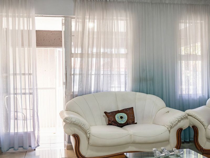 A bright living room featuring tiled flooring and a sliding glass door leading to an outdoor area, finished with sheer curtains.