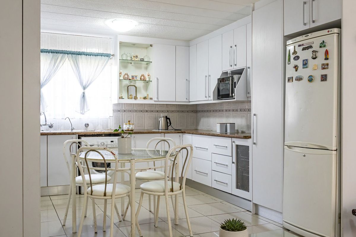 A functional kitchen featuring white cabinetry, laminate countertops, tiled backsplash, and integrated laundry plumbing, offering a clean and practical layout for daily use.