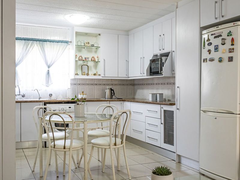 A functional kitchen featuring white cabinetry, laminate countertops, tiled backsplash, and integrated laundry plumbing, offering a clean and practical layout for daily use.