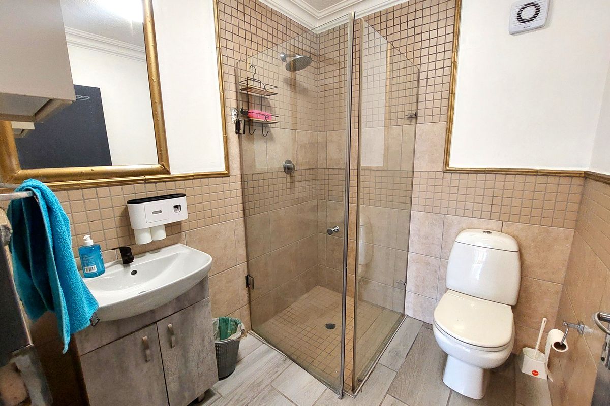 A functional bathroom featuring a glass-enclosed shower, vanity cabinet with basin, and toilet, finished with neutral wall and floor tiling.