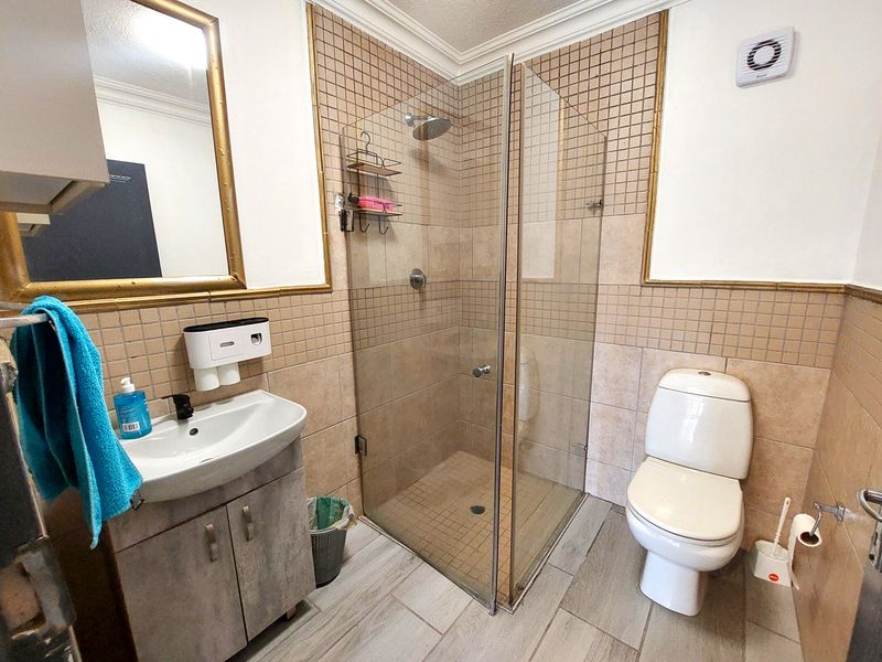 A functional bathroom featuring a glass-enclosed shower, vanity cabinet with basin, and toilet, finished with neutral wall and floor tiling.
