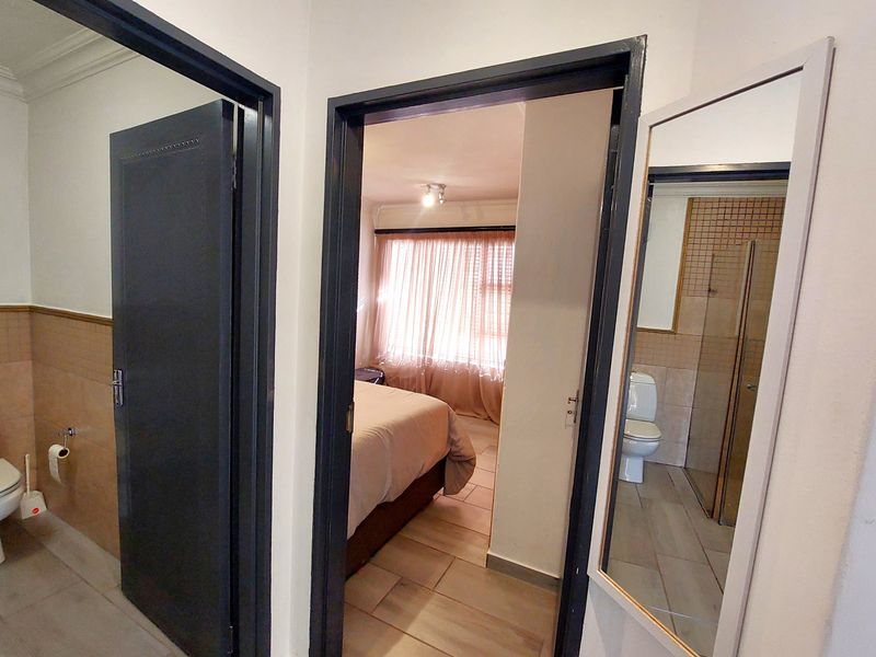 A hallway providing access to a bedroom and a bathroom, featuring neutral tiled flooring and dark-painted door frames.