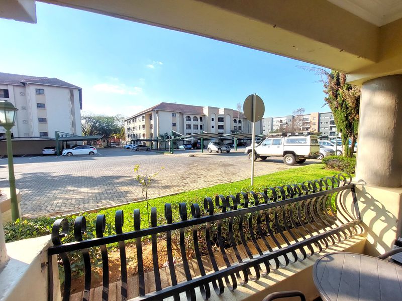 A view from a covered balcony overlooking a paved apartment complex parking area with carports and landscaped surroundings.