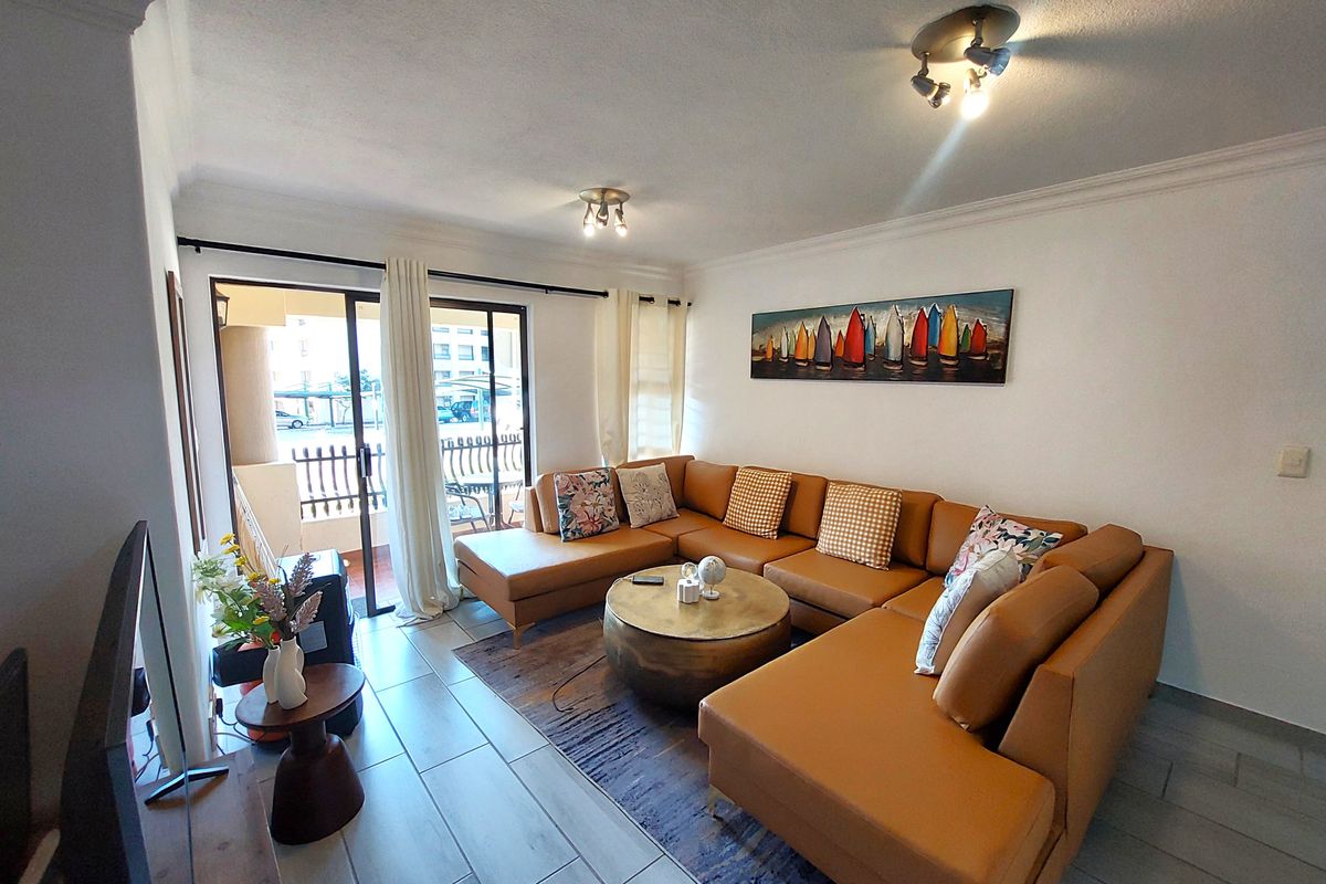A bright and well-maintained living room featuring tiled flooring, coved ceilings, and a sliding glass door providing access to an outdoor balcony area.