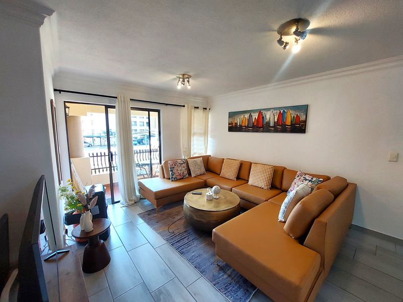 A bright and well-maintained living room featuring tiled flooring, coved ceilings, and a sliding glass door providing access to an outdoor balcony area.