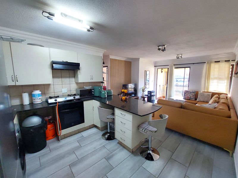 Open-plan living area featuring a functional kitchen with granite countertops, gas hob, and tiled flooring, seamlessly flowing into the adjacent lounge space.