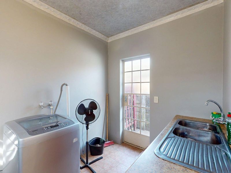Functional laundry room featuring a double bowl stainless steel sink, laminate countertop, tiled flooring, and direct access to the exterior.