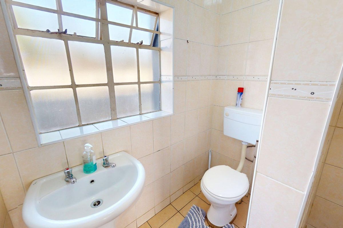 A compact bathroom featuring a pedestal basin, ceramic toilet, and full-height wall tiling with a steel-framed window.