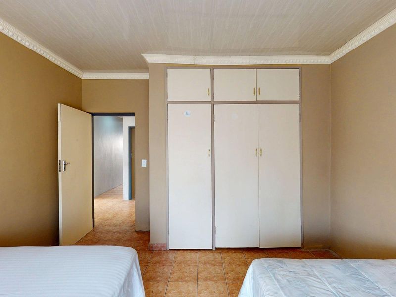A bedroom featuring built-in cupboards, tiled flooring, and decorative ceiling cornicing, offering a functional space with potential for cosmetic updates.