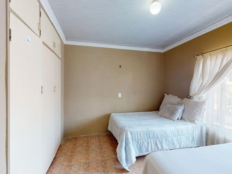 A bedroom featuring tiled flooring, built-in cupboards, and decorative ceiling cornicing, offering a functional space with potential for cosmetic updates.