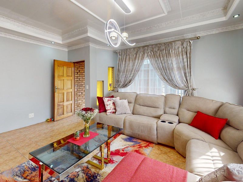 A well-maintained living room featuring a tray ceiling with recessed lighting, tiled flooring, and an exposed brick accent wall.