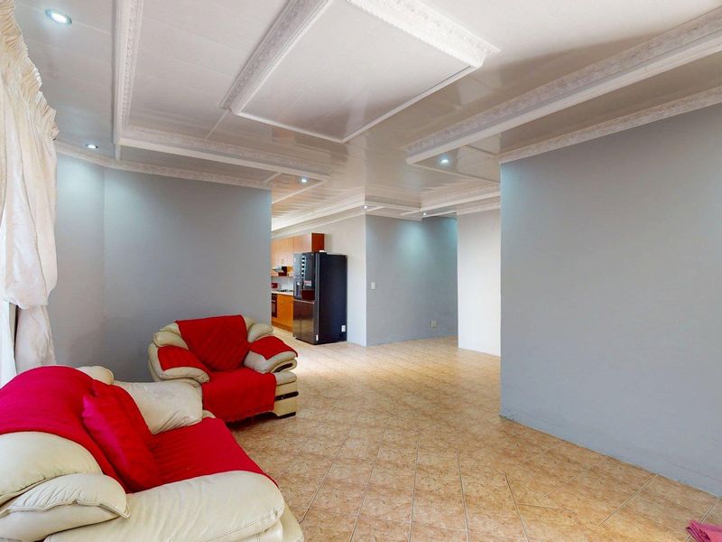 An open-plan living area featuring tiled flooring, decorative ceiling molding, and recessed lighting, with a view through to the kitchen area.