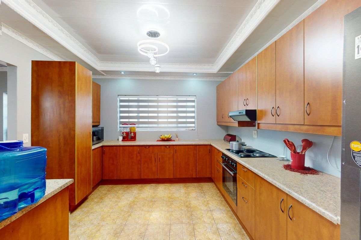 A functional U-shaped kitchen featuring wood-look cabinetry, laminate countertops, built-in oven, hob, extractor fan, and tiled flooring with decorative coved ceiling detail.