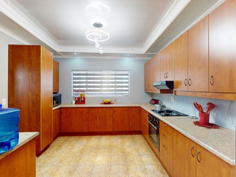 A functional U-shaped kitchen featuring wood-look cabinetry, laminate countertops, built-in oven, hob, extractor fan, and tiled flooring with decorative coved ceiling detail.