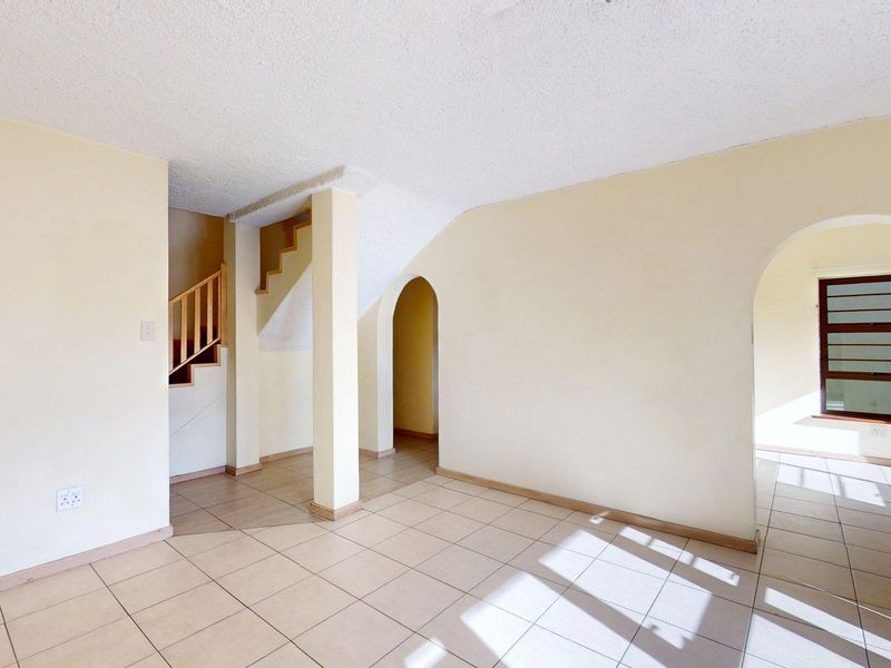 An empty, open-plan living area featuring tiled floors, arched architectural details, and a staircase leading to the upper level.