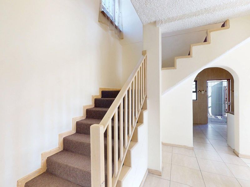 Entrance hallway featuring a staircase with wooden balustrade, tiled flooring, and an arched doorway leading to the rear of the townhouse.