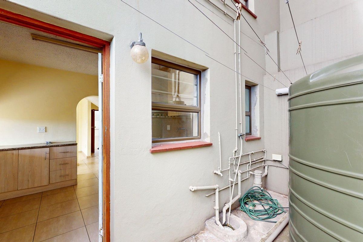 Rear exterior view showing a water tank, exposed plumbing, and a direct entrance into the kitchen area with tiled floors and wooden cabinetry.